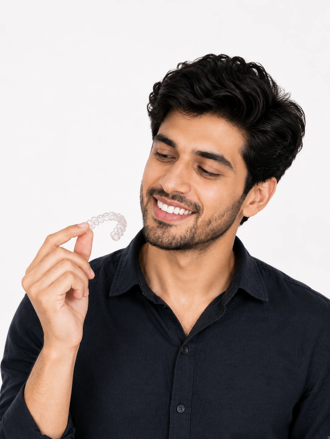 Man smiling while looking at a clear aligner tray he is holding
