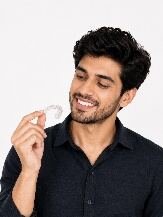 Patient smiling while holding a clear aligner tray